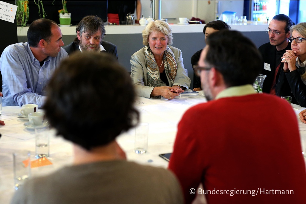 Foto von Monika Grütters, die mit Teilnehmern an einem Tisch sitzt und mit ihnen diskutiert.