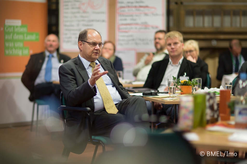 Foto von Christian Schmidt, der an einem Tisch sitzt und mit den Teilnehmern diskutiert.