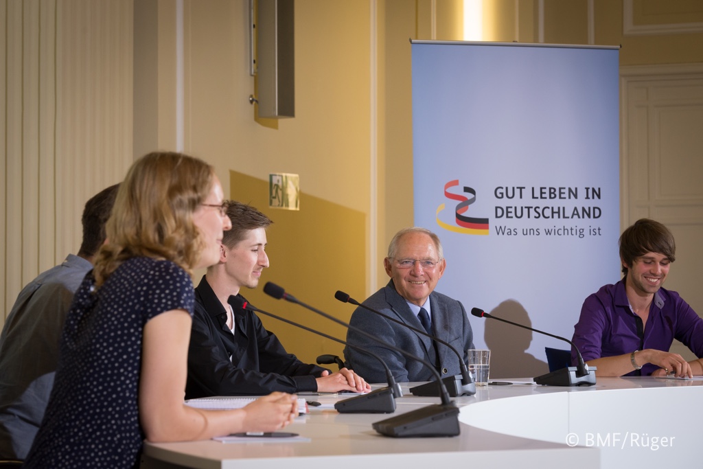 Foto von Wolfgang Schäuble auf einem Podium mit drei Teilnehmern.